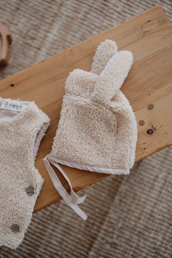 Driedelige teddyset voor baby's in beige, inclusief vest, muts en anit-slip slofjes, beschikbaar in maten 0-12 maanden en 12-24 maanden.