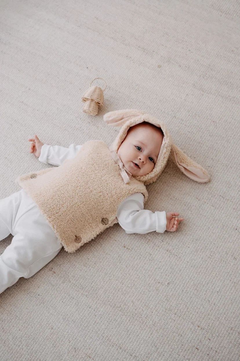 Driedelige teddyset voor baby's in beige, inclusief vest, muts en anit-slip slofjes, beschikbaar in maten 0-12 maanden en 12-24 maanden.
