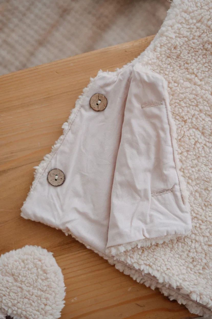 Driedelige teddyset voor baby's in ecru, inclusief vest, muts en anit-slip slofjes, beschikbaar in maten 0-12 maanden en 12-24 maanden.